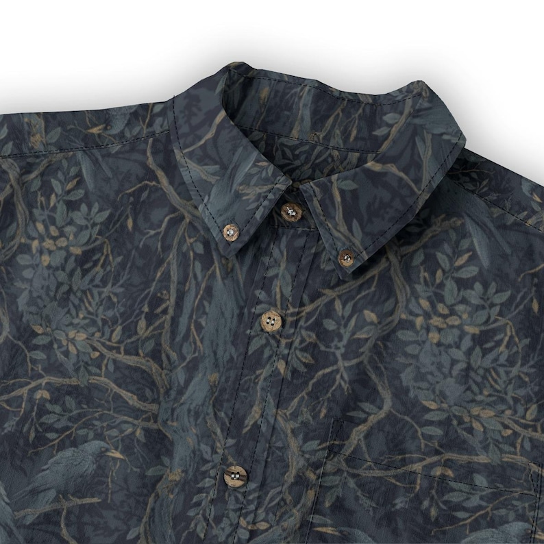 May include: A button-down shirt featuring a dark navy blue background with a repeating pattern of tree branches, leaves, and birds in muted shades of gray, brown, and dark green. The shirt has a pointed collar and light brown circular buttons.