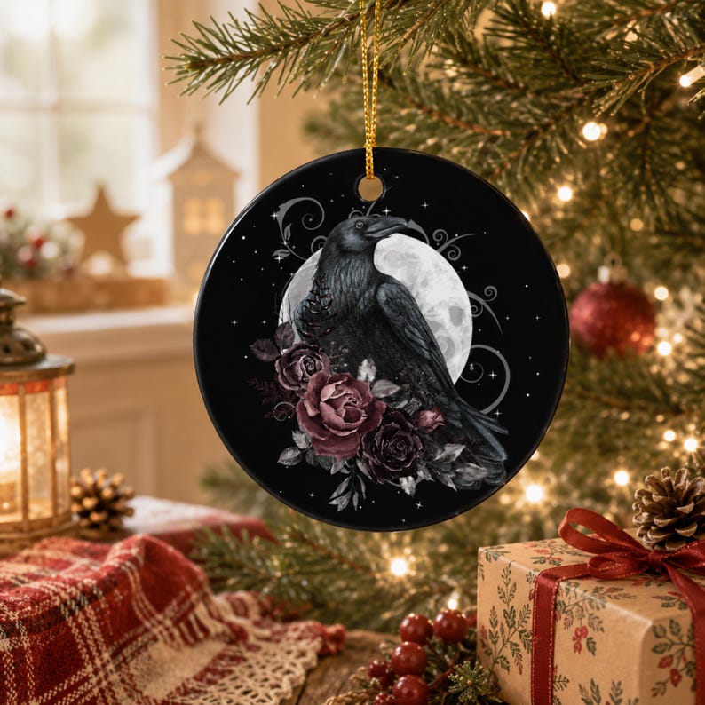 May include: A round black ceramic ornament featuring a detailed illustration of a raven perched before a full moon, accented with dark red and purple roses and delicate swirling vine patterns, suspended by a thin gold cord for hanging.
