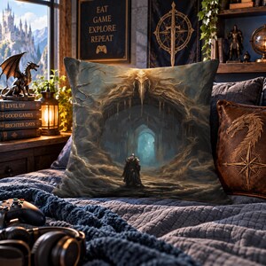 May include: A square throw pillow featuring a detailed fantasy illustration of a lone armored figure standing before a dark, cavernous stone archway with glowing blue light in the distance, rendered in shades of brown, gold, and deep blue.