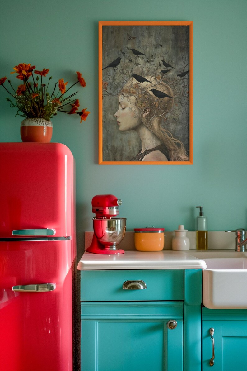May include: A kitchen scene featuring a bright red retro refrigerator, a red stand mixer, and teal cabinets. A framed print of a person with birds in their hair hangs on the wall above a white sink, next to a vase of orange flowers.