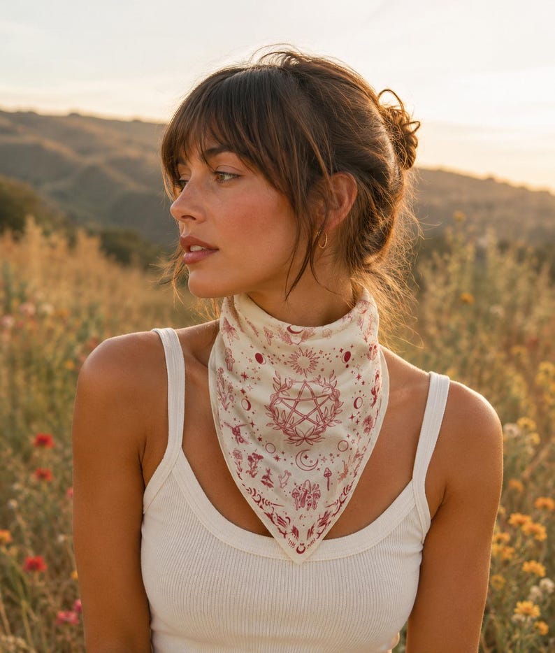 May include: A triangular bandana in off-white fabric featuring a detailed maroon-colored print. The design includes a central pentagram surrounded by celestial motifs, including suns, moons, stars, and various botanical elements like mushrooms.