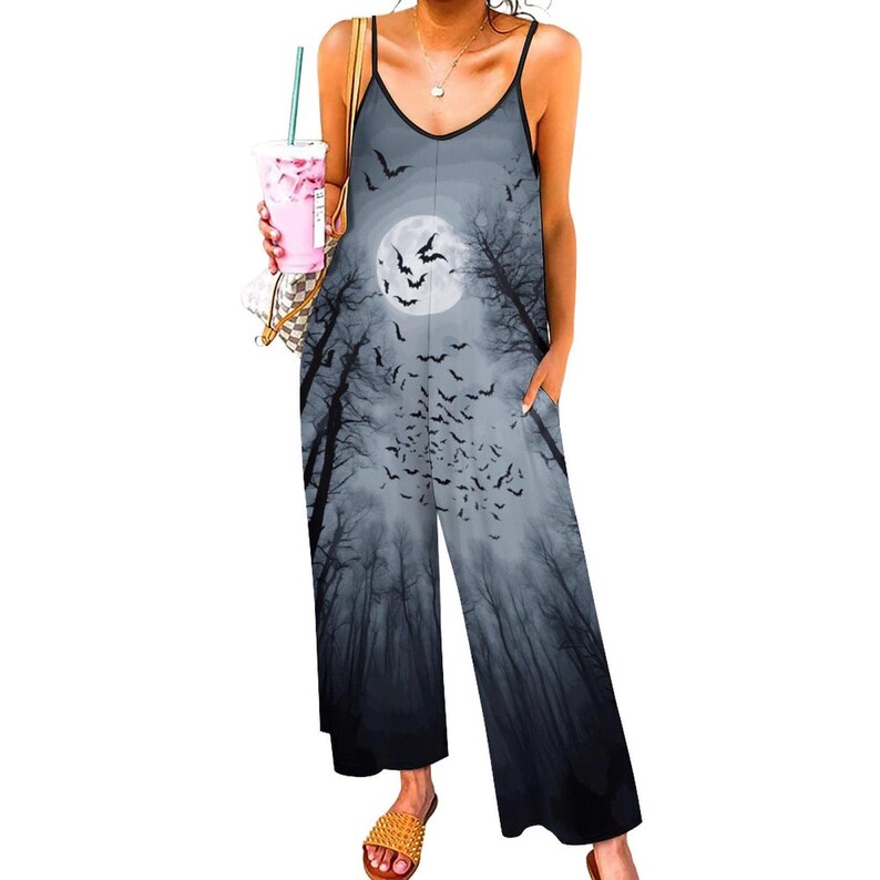 May include: A sleeveless jumpsuit featuring a gray and black graphic print of a full moon, silhouetted trees, and a flock of bats. The garment has thin spaghetti straps, a V-neckline, and wide-leg trousers with side pockets, creating a loose silhouette.