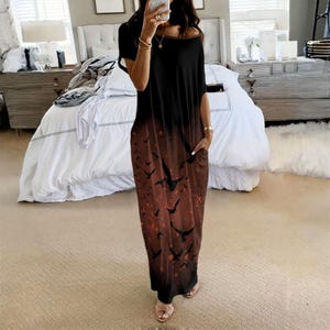 May include: A short-sleeved maxi dress featuring a black top that transitions into a dark brown bottom. The lower portion of the dress is decorated with a repeating pattern of black bird silhouettes and small orange speckles. It includes side pockets.