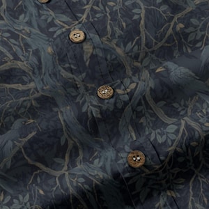 May include: A dark blue button-down shirt featuring a repeating pattern of tree branches, leaves, and birds. The garment includes a vertical placket with three visible round, textured, light brown wooden buttons stitched in a centered alignment.