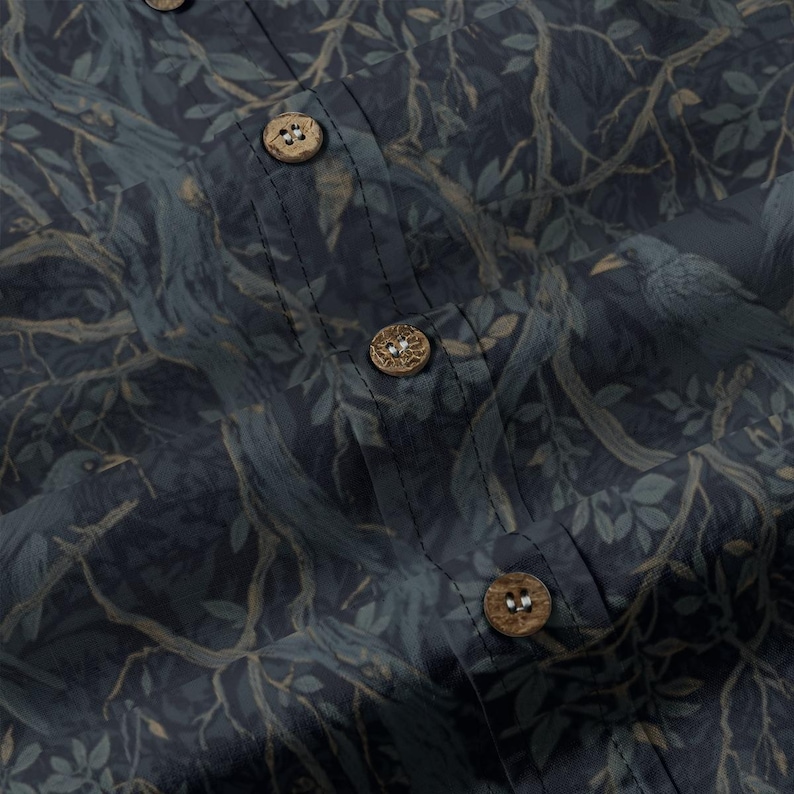 May include: A dark blue button-down shirt featuring a repeating pattern of tree branches, leaves, and birds. The garment includes a vertical placket with three visible round, textured, light brown wooden buttons stitched in a centered alignment.