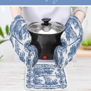 May include: A pair of oven mitts and a square pot holder featuring a blue and white toile de jouy pattern depicting landscape scenes. The mitts are shown holding a black electric pot with a glass lid and a red power switch on the front.