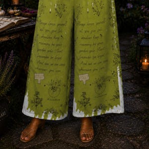 May include: Wide-leg pants in olive green featuring a dark green botanical print with text that reads: Always honor yourself all you give leads shoulder keep rosemary by your garden gate Plant lavender be loyal And like we live cards wherever you can.