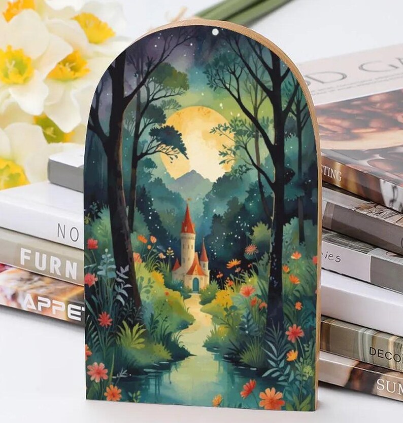 May include: Wooden arched wall art featuring a watercolor painting of a fairytale castle in a forest. The artwork depicts a full moon, a river, and colorful flowers. The castle has red-roofed towers.