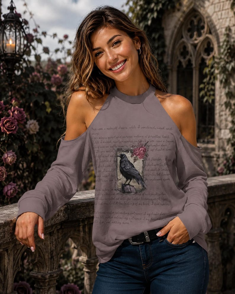 May include: A mauve cold-shoulder long-sleeve top featuring a graphic print of a black raven perched on a wooden post, surrounded by pink roses and overlaid with cursive script text that reads Once upon a midnight dreary while I pondered weak and weary.