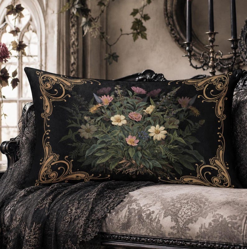 May include: A rectangular throw pillow featuring a black background with a central botanical illustration of various flowers in shades of pink, yellow, and white, surrounded by a decorative gold-colored filigree border on all four corners.