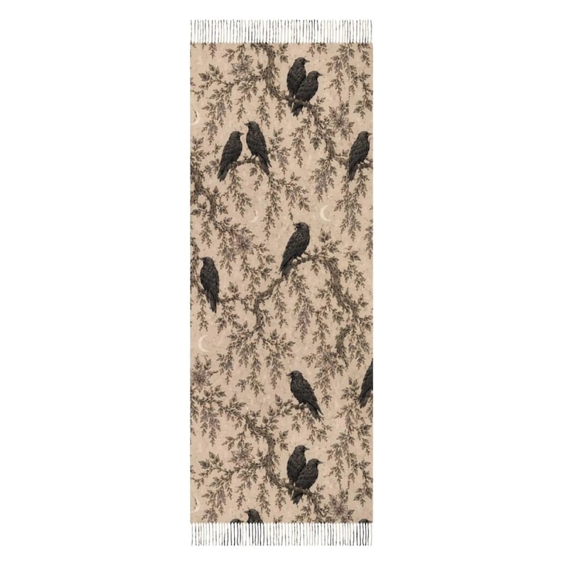 Op de afbeelding: Een rechthoekige sjaal met een beige achtergrond en een herhalend patroon van zwarte vogels op donkerbruine boomtakken. Het ontwerp bevat kleine halve maantjes verspreid tussen het gebladerte en is afgewerkt met franjes aan de uiteinden.