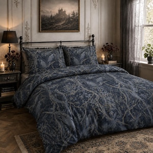 Pode incluir: Uma capa de edredão azul-escura e duas fronhas a condizer com um padrão detalhado de corvos pousados e ramos de árvore intrincados em tons de cinzento suaves. O conjunto de cama está disposto numa cama com estrutura de metal preto.