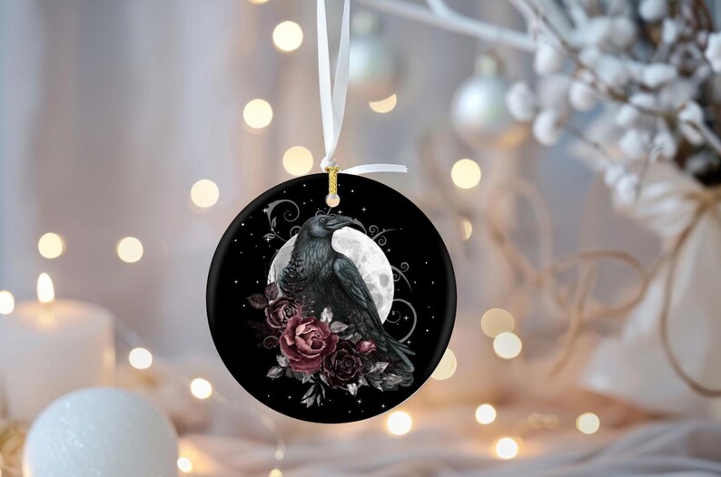 May include: A round ceramic ornament featuring a black raven perched in front of a full moon, surrounded by dark red and purple roses. The design is set against a black background with swirling silver accents and hangs from a white ribbon.