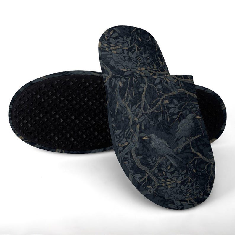 May include: A pair of slip-on slippers featuring a dark navy and black pattern of crows perched on tree branches with leaves. The soles are black with a textured, non-slip grip surface, and the upper fabric displays a detailed botanical illustration.
