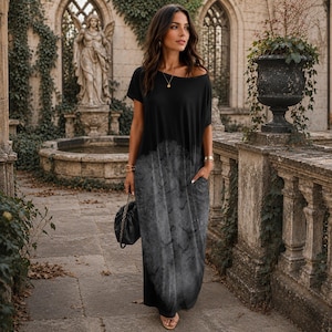 May include: A floor-length maxi dress featuring a solid black short-sleeved bodice that transitions into a grey, mottled, cloud-like print on the skirt. The garment includes a wide neckline, short sleeves, and side pockets, with a loose, flowing fit.