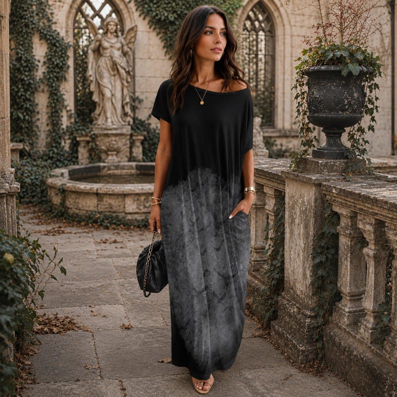 May include: A floor-length maxi dress featuring a solid black short-sleeved bodice that transitions into a grey, mottled, cloud-like print on the skirt. The garment includes a wide neckline, short sleeves, and side pockets, with a loose, flowing fit.