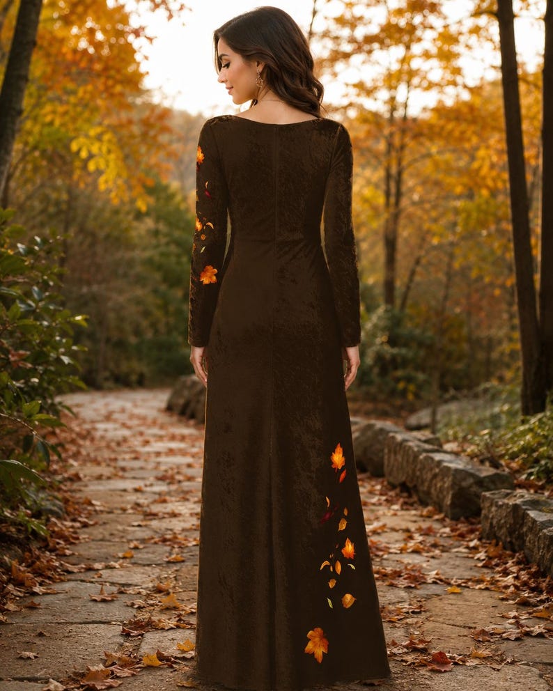 May include: A floor-length dark brown long-sleeve dress featuring a subtle velvet-like texture. The garment is adorned with embroidered orange and yellow autumn leaf motifs scattered along the right sleeve and the lower left side of the skirt.