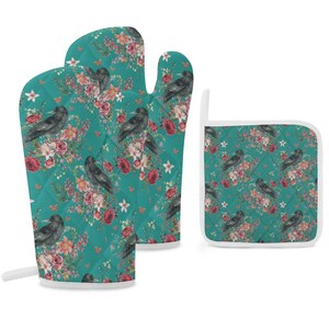 May include: A quilted oven mitt and a square pot holder featuring a teal background with a repeating pattern of black crows, deep red roses, and light pink flowers. Both items have white trim and a small loop for hanging on the side of the pieces.