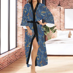 May include: A blue kimono robe with a botanical pattern featuring leaves and butterflies in shades of brown and gold. The robe has a black satin trim and a matching belt. The sleeves are wide, and the robe is open in the front.