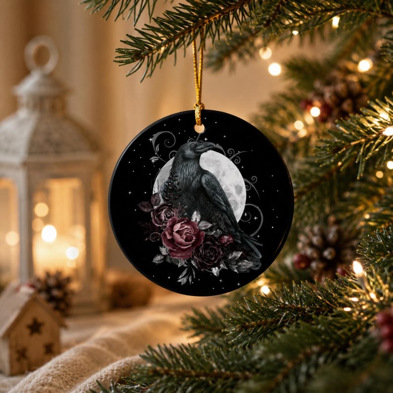 May include: A round ceramic ornament featuring a black raven perched in front of a full moon, surrounded by dark red roses and swirling decorative lines. The ornament is black with a glossy finish and hangs from a thin gold cord.