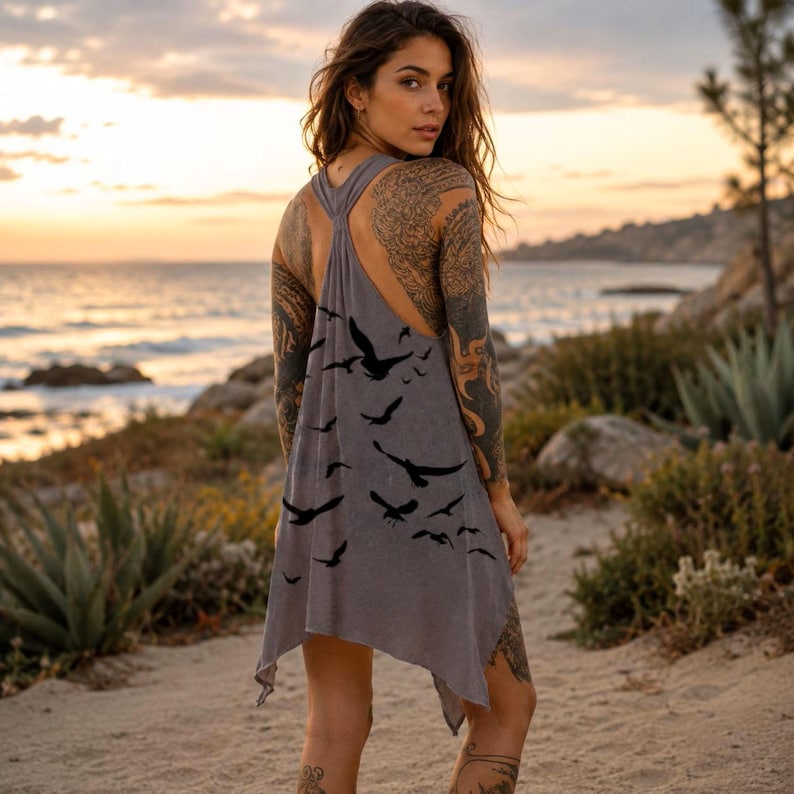 May include: A grey sleeveless tank top with a racerback design and an asymmetrical hemline. The garment features a black graphic print of multiple flying birds scattered across the back. The fabric has a soft, slightly worn texture and appearance.