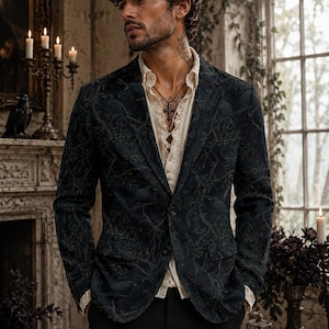 Pode incluir: Um blazer azul-marinho escuro com um padr&atilde;o tonal e intrincado de aves e motivos bot&acirc;nicos, usado sobre uma camisa de bot&otilde;es cor de creme com gola de folhos e um pendente de cruz prateada, combinado com cal&ccedil;as pretas lisas.
