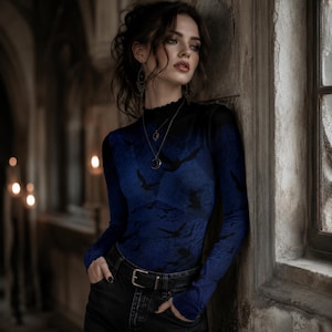 May include: A long-sleeved mock neck top featuring a gradient blue and black color scheme with a repeating silhouette pattern of flying birds. The garment has a fitted silhouette and a ruffled neckline, paired with black denim jeans and a black belt.
