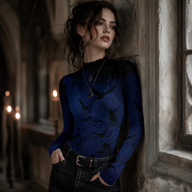 May include: A long-sleeved mock neck top featuring a gradient blue and black color scheme with a repeating silhouette pattern of flying birds. The garment has a fitted silhouette and a ruffled neckline, paired with black denim jeans and a black belt.