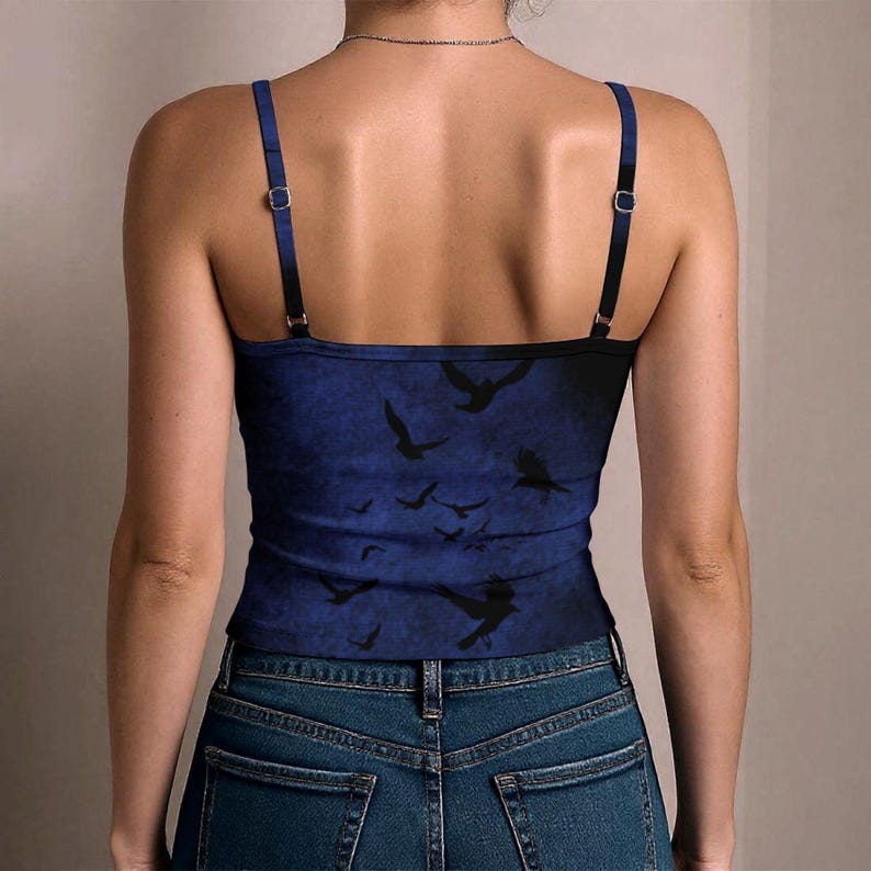 May include: A blue camisole top featuring a dark, mottled background pattern with silhouettes of flying birds. The garment has thin, adjustable shoulder straps with silver-toned metal sliders and a straight neckline, worn with blue denim jeans.