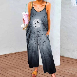 May include: A sleeveless jumpsuit featuring a gray and black gradient print of a full moon, silhouetted trees, and a flock of flying bats. The garment has thin spaghetti straps, a V-neckline, and wide-leg trousers with side pockets.