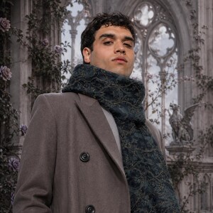 Peut inclure: Un manteau taupe &agrave; double boutonnage port&eacute; avec une &eacute;charpe bleu sarcelle fonc&eacute; orn&eacute;e d'un motif botanique complexe dans des tons dor&eacute;s et verts. L'&eacute;charpe est enroul&eacute;e autour du cou, superpos&eacute;e sur une chemise gris clair, cr&eacute;ant un aspect textur&eacute;.