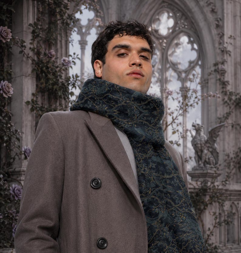 Peut inclure: Un manteau taupe &agrave; double boutonnage port&eacute; avec une &eacute;charpe bleu sarcelle fonc&eacute; orn&eacute;e d'un motif botanique complexe dans des tons dor&eacute;s et verts. L'&eacute;charpe est enroul&eacute;e autour du cou, superpos&eacute;e sur une chemise gris clair, cr&eacute;ant un aspect textur&eacute;.