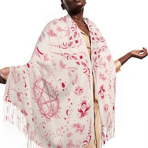 May include: Cream-coloured shawl featuring a repeating pattern of red celestial and botanical illustrations. The design includes stars, moons, mushrooms, and a pentagram. The shawl has a fringed edge.