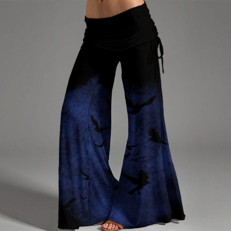 May include: Wide-leg pants featuring a high-waisted black band with side ties. The lower portion of the pants transitions into a deep blue gradient with a dark, textured pattern of silhouettes resembling flying birds across the fabric surface.