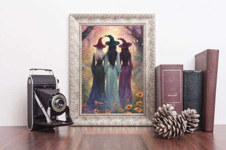 May include: A framed art print depicting three figures wearing pointed hats and long dresses standing in a forest clearing filled with flowers. The figures are shown from behind, with one in a dark dress, one in light blue, and one in purple.