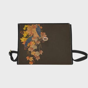 May include: A rectangular dark brown bag featuring a printed design of two black crows perched among vibrant autumn maple leaves in shades of yellow, orange, and red. The bag includes black side straps and a centered oval metallic clasp detail.