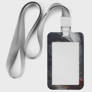 Puede incluir: Un porta credencial rectangular vertical con un cord&oacute;n de tela gris claro. El porta credencial presenta un estampado gr&aacute;fico de bosque oscuro con tonos apagados y un peque&ntilde;o acento rojo en la esquina inferior derecha, rodeando una ventana transparente.