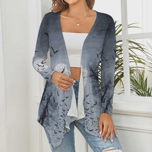 May include: A long-sleeve open-front cardigan featuring a gray and white gradient print of a full moon, bare tree silhouettes, and numerous flying bats. The garment has a draped, asymmetrical hemline and is worn over a plain white tube top.