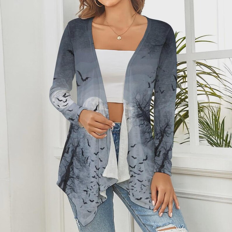 May include: A long-sleeve open-front cardigan featuring a gray and white gradient print of a full moon, bare tree silhouettes, and numerous flying bats. The garment has a draped, asymmetrical hemline and is worn over a plain white tube top.