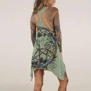 May include: A sage green racerback tank top featuring a graphic print of a crescent moon, swirling vines, small stars, and various mushrooms. The garment has an asymmetrical hemline and a loose, flowing fit that hangs from the shoulders.