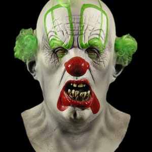 May include: A creepy clown mask with a white face, green hair, and a red nose. The clown has a wide, toothy grin and a menacing expression.
