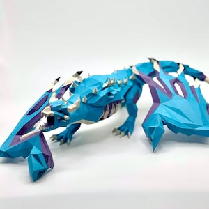 May include: A geometric papercraft dragon sculpture in shades of blue, purple, and white. The dragon has a detailed, angular design with open wings and sharp teeth. The sculpture is set against a plain white background.