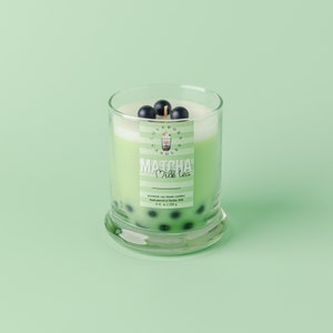 May include: A clear glass candle with a green Matcha Milk Tea scent. The candle has a white top and is decorated with dark blue spheres, resembling boba. The label reads "Matcha Milk Tea" and "Love Boba Candles". The candle is 9 fl oz / 255 g.