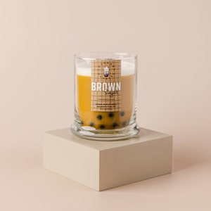 May include: A glass jar candle with a brown sugar scent. The candle is topped with a layer of white wax and has a label that says "BROWN Sugar". The jar is filled with small black boba pearls.