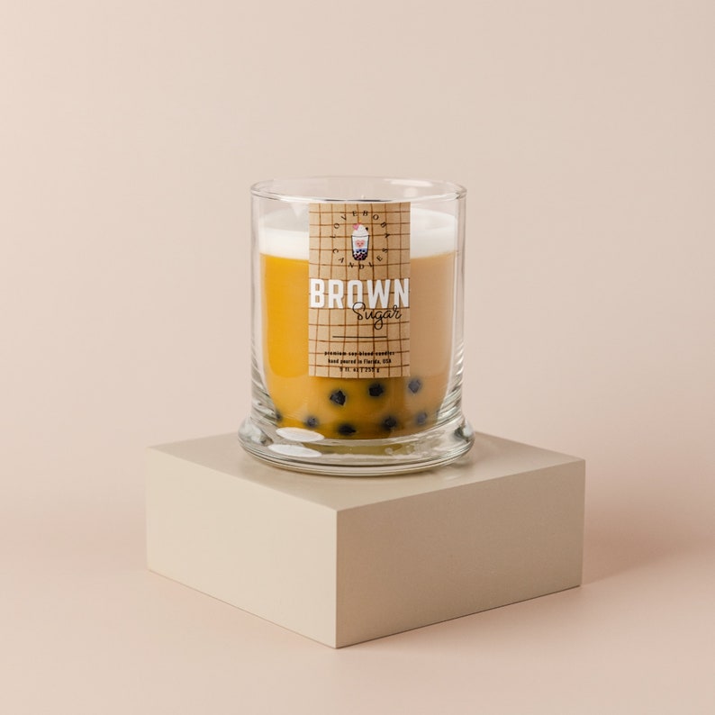 May include: A glass jar candle with a brown sugar scent. The candle is topped with a layer of white wax and has a label that says "BROWN Sugar". The jar is filled with small black boba pearls.