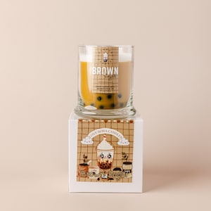 May include: A brown sugar boba candle in a clear glass jar with a white lid. The jar is sitting on a white box with a brown and white checkered pattern. The box has the text "I Love Boba Candles" and "Brown Sugar" on it. The candle has a brown sugar scent and is decorated with boba pearls.