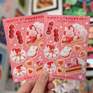 May include: Two pink sticker sheets with the text "MIFFY STRAWBERRY STICKER SHEET" and illustrations of strawberries, bunny characters, and desserts. The stickers are held by a hand.