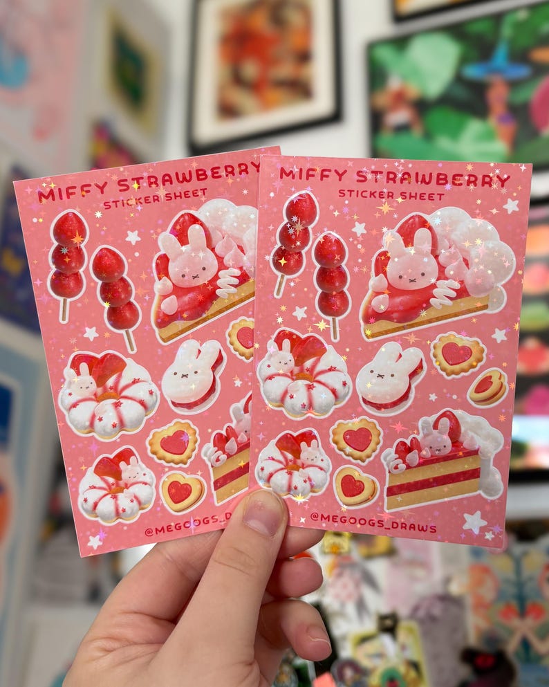 May include: Two pink sticker sheets with the text "MIFFY STRAWBERRY STICKER SHEET" and illustrations of strawberries, bunny characters, and desserts. The stickers are held by a hand.