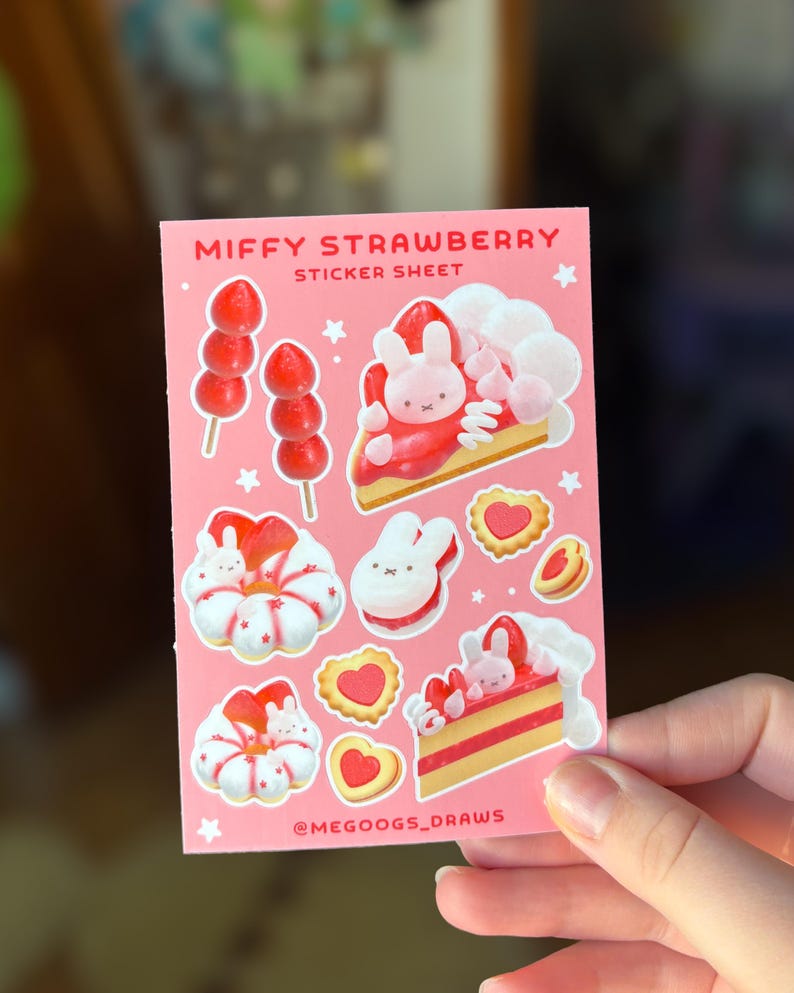 May include: A pink sticker sheet featuring illustrations of a bunny character and strawberry-themed treats. The sheet includes images of strawberry skewers, cake slices, and heart-shaped cookies. Text on the sheet reads "MIFFY STRAWBERRY STICKER SHEET" and "@MEGOOGS_DRAWS".