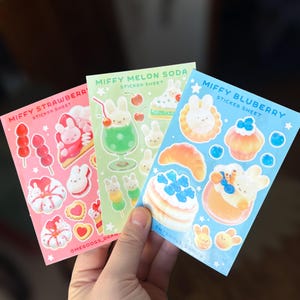May include: Three sticker sheets featuring illustrations of a bunny character with food and drink themes. The sheets are labeled "Miffy Strawberry", "Miffy Melon Soda", and "Miffy Bluberry". Each sheet has a different color background.